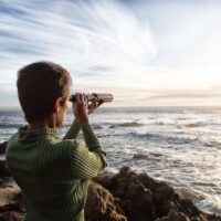 person with spyglass looks at ocean horizon
