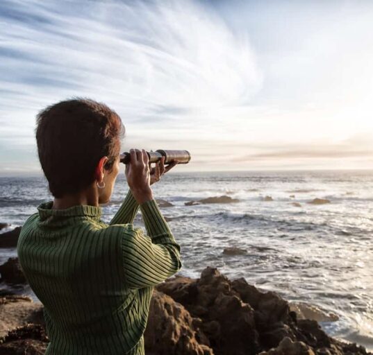 person with spyglass looks at ocean horizon